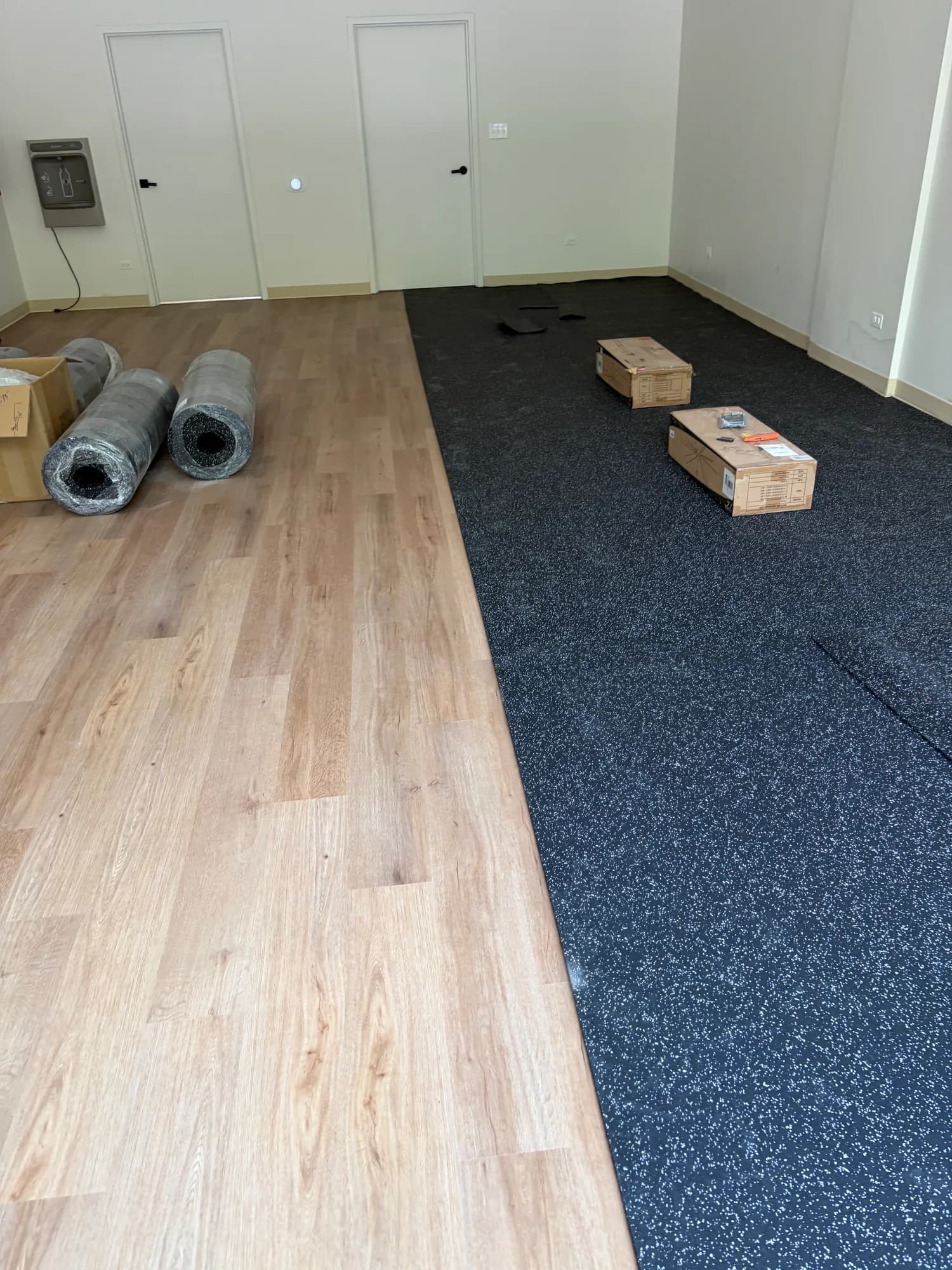 Rubber gym flooring half installed, meeting the original plank floor along a straight seam