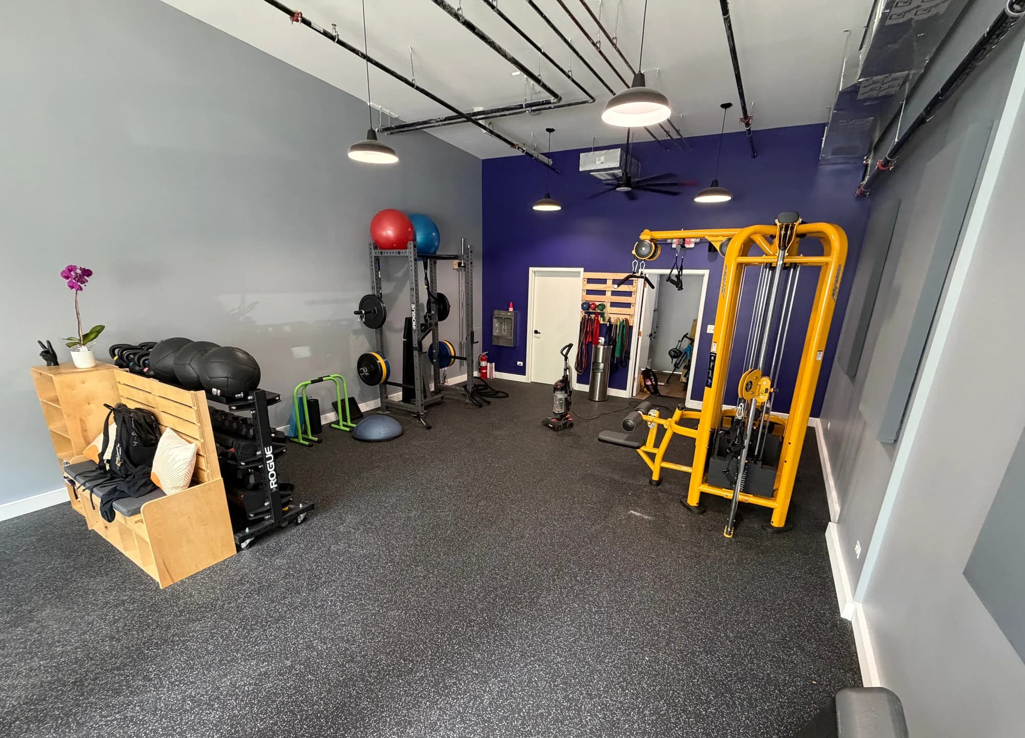 Finished fitness studio with rubber flooring, custom bench seating, squat rack, and cable machine