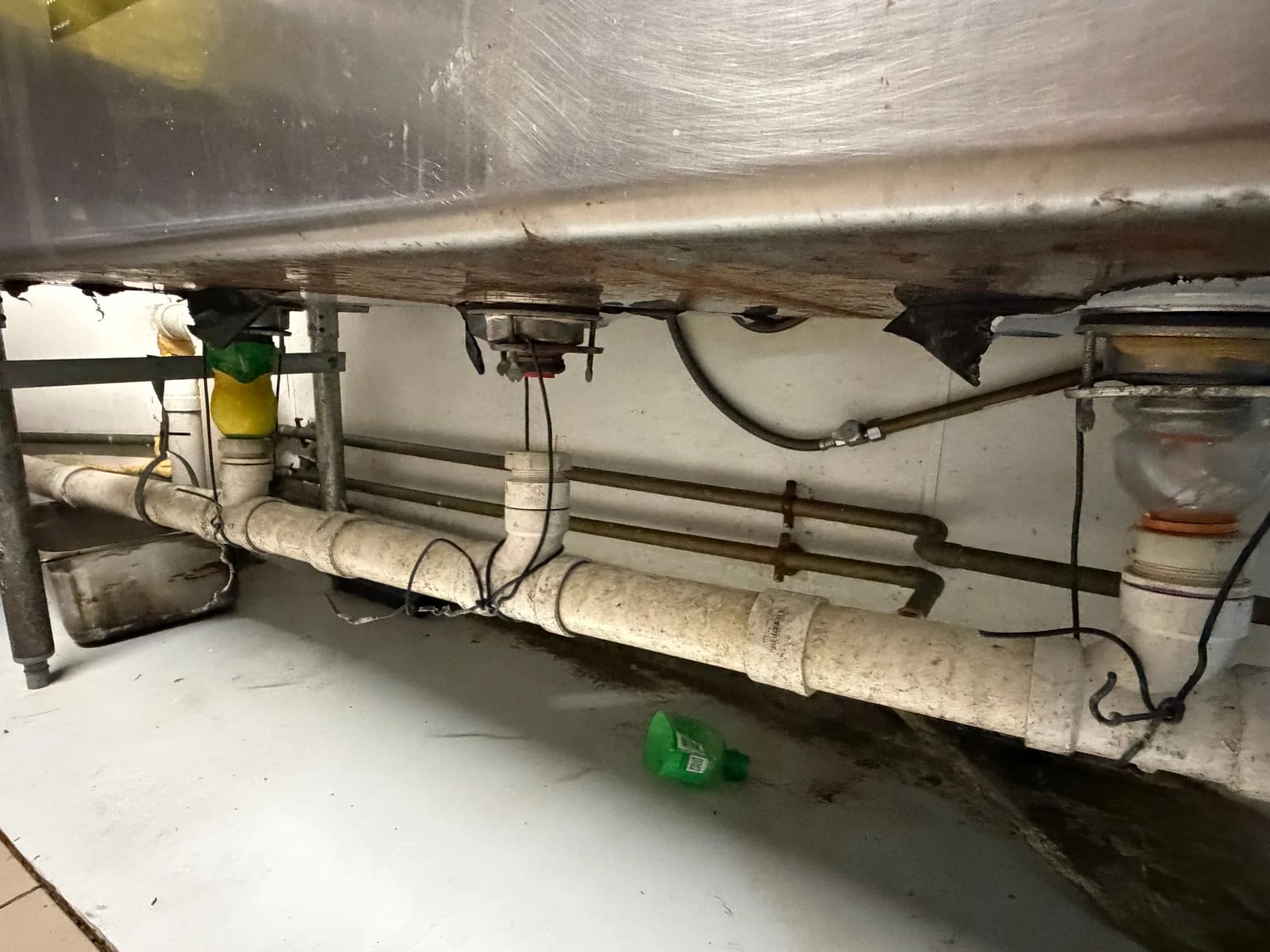 Corroded and broken drain tailpieces under a stainless commercial three-bay sink